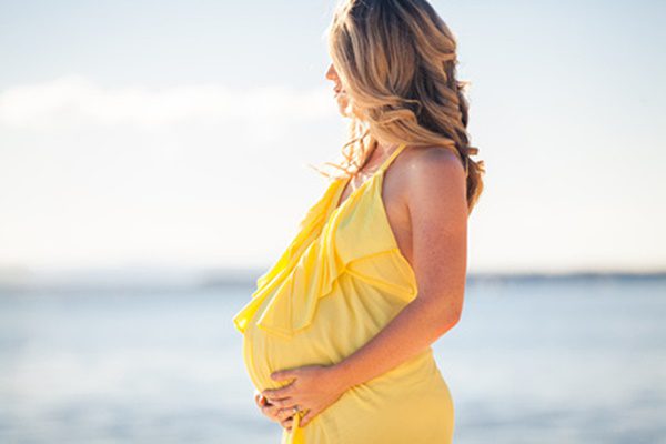 Profile view of pregnant woman in yellow dress on the beach