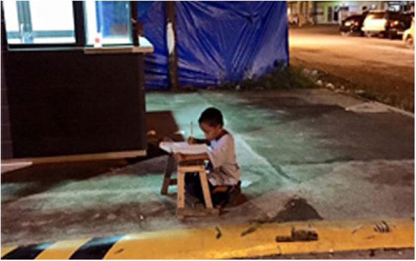 Filipijski chłopiec odrabia pracę w świetle restaurycyjnej witryny. The telegraph