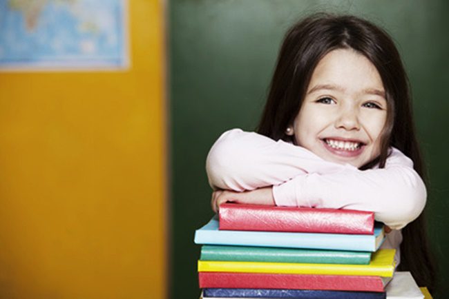 Happy little girl with books in school