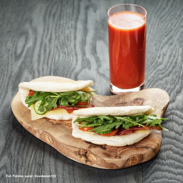 rustic sandwiches with ham arugula and tomatoes in pita bread and glass of juice, on wood table