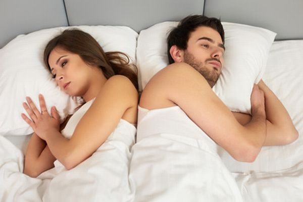 Upset couple lying back to back in bed