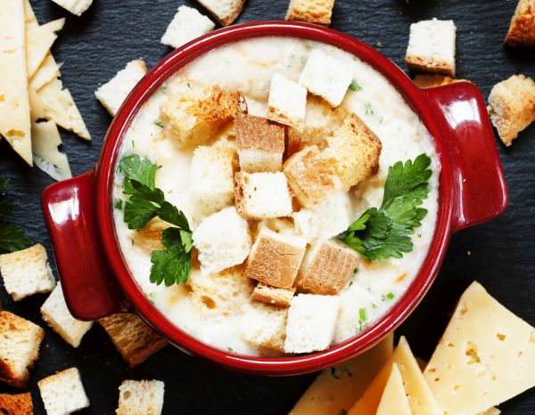 Cheese soup with croutons in red portioned saucepan, top view