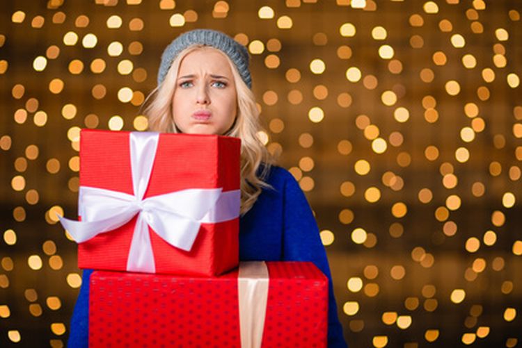 Portrait of a sad woman holding gift boxes over holidays lights background