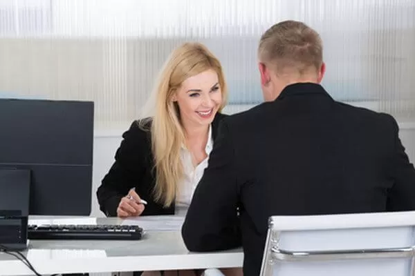Smiling young businesswoman interviewing male candidate at desk in office