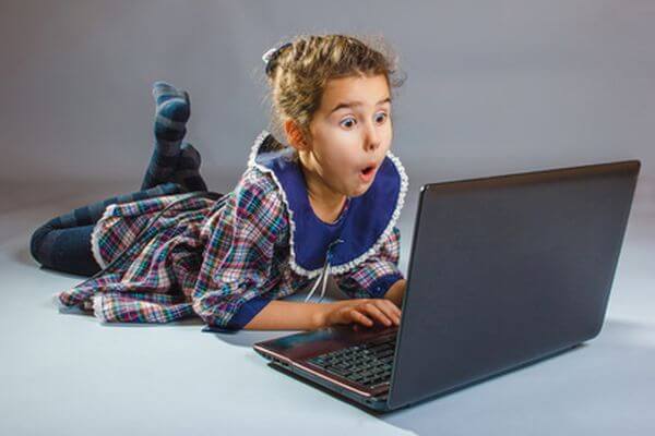 the girl child is playing in a laptop surprised on a gray background