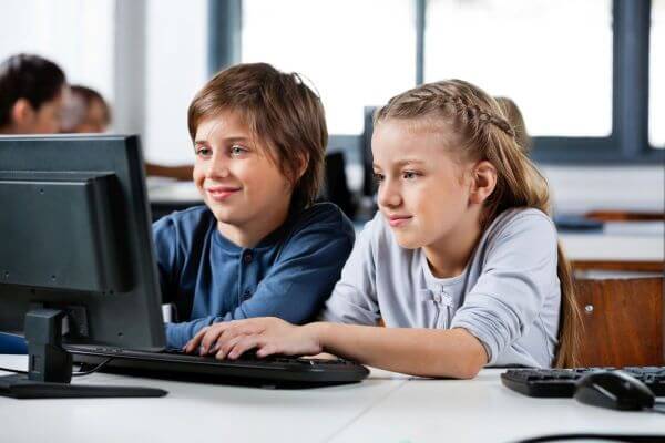 Cute little boy and girl using desktop PC at desk in school computer lab