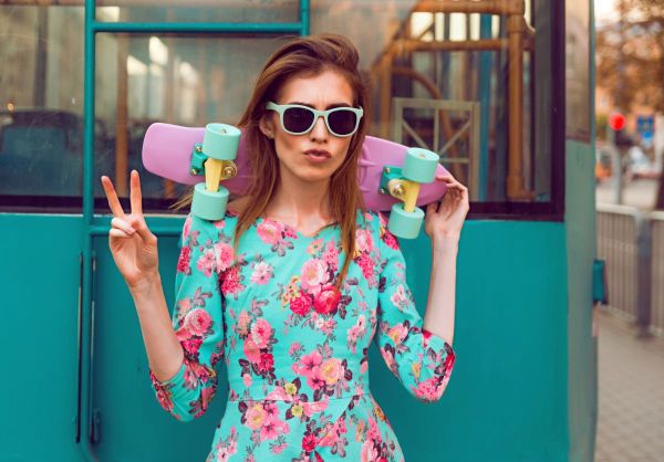 Beautiful hipster fashion young woman model posing with a pink skateboard on city background