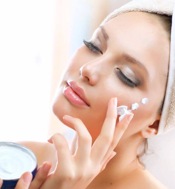 Beautiful Young Woman applying facial moisturizing cream