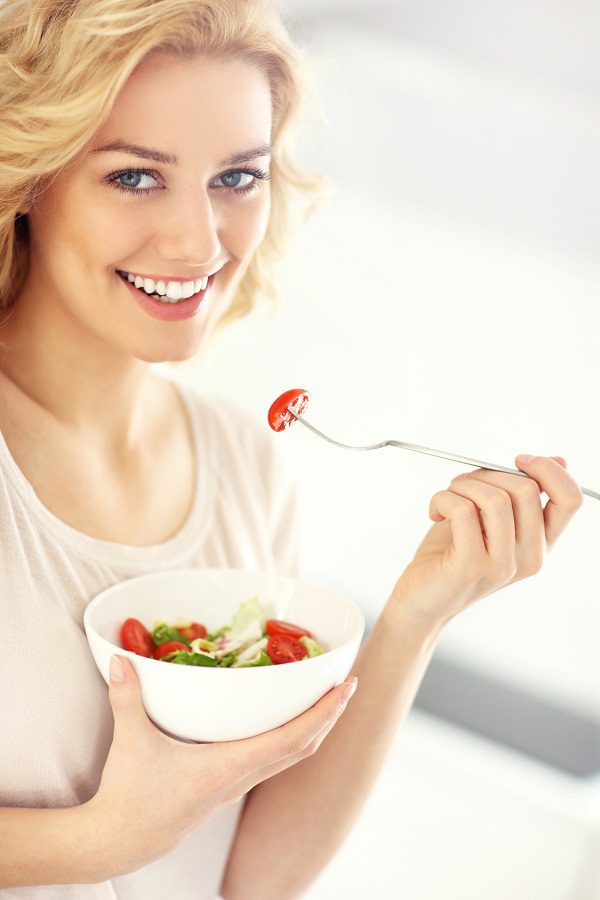 A picture of a young woman eating salad in the kitchen