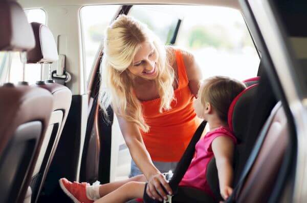 family, transport, safety, road trip and people concept - happy mother fastening child with car seat belt