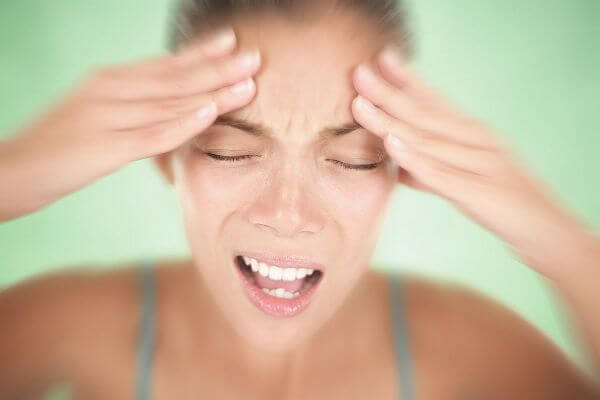 Woman having a migraine / headache holding her head in pain and stress. Shallow depth of field on green background.