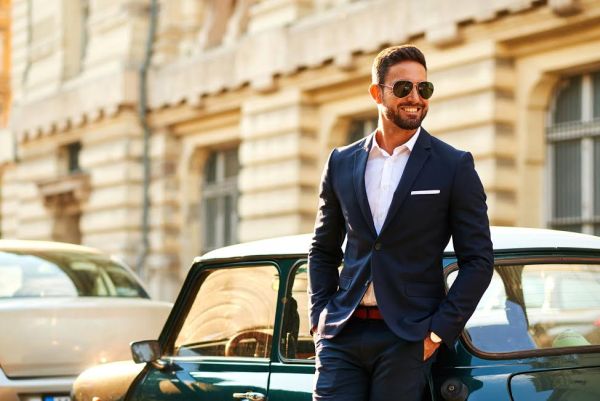 A handsome young businessman smiling and standing next to his car