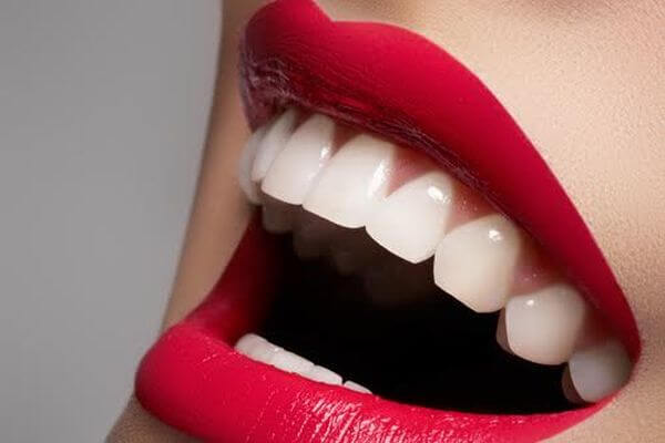 Close-up happy female smile with healthy white teeth, bright magenta lips make-up. Cosmetology, dentistry and beauty care.