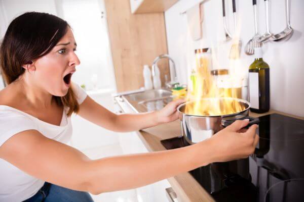 Shocked Young Woman Looking At Burnt Food In Cooking Pot
