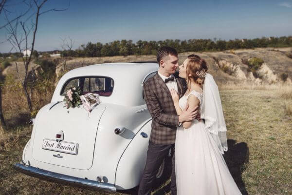 The bride and groom have fun behind the wheel of retro car. Wedding